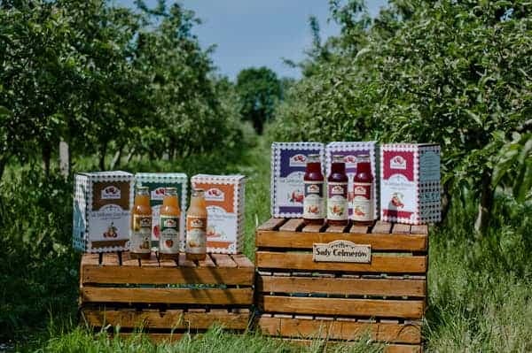 Soki i kartony Sady Celmerów na drewnianych skrzynkach wśród jabłoni